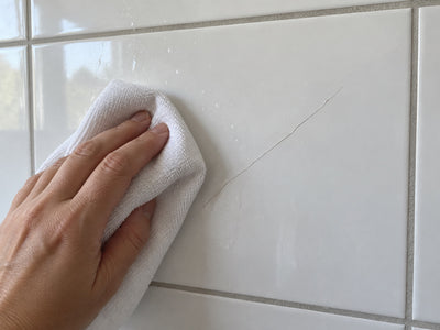 Hand veegt een witte tegel met een scheur schoon